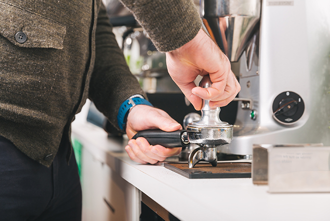 metal tamper of a portafilter pushing coffee grounds down into a neat little puck